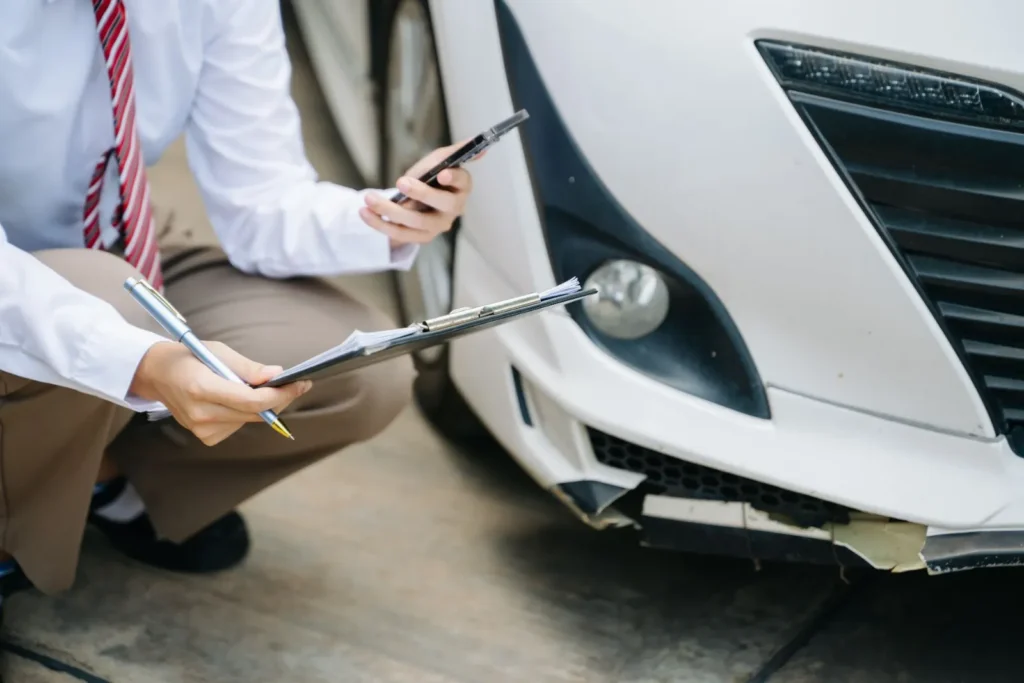 Mann begutachtet den Autoschaden und telefoniert mit dem Handy