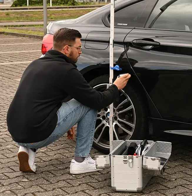 Gutachter kniet an einem Fahrzeugrad mit Messkoffer