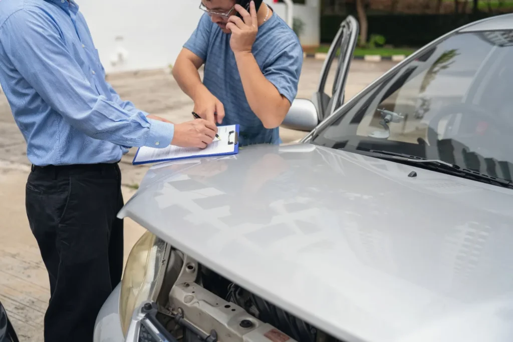 Zwei Männer besprechen Unterlagen an einem Auto mit beschädigter Motorhaube